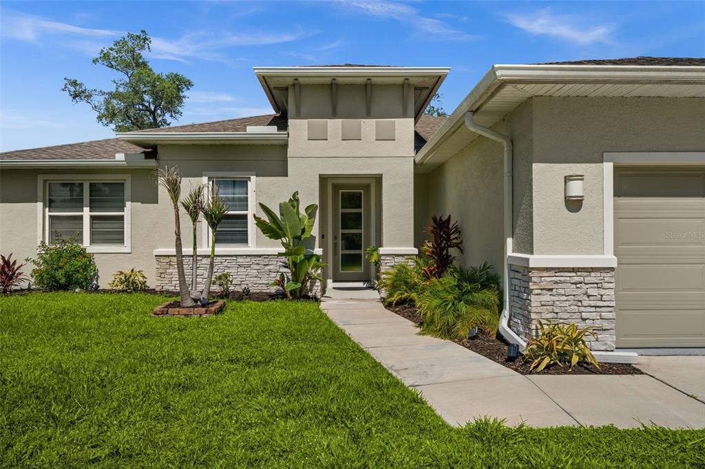 The exterior of a single-story house features a tan stucco facade, stone accents, and a walkway — 4831 OCALA TERRACE, NORTH PORT, FL