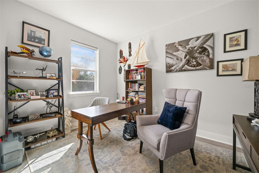 A home office features a wooden desk, a gray armchair, bookshelves, and aviation-themed wall art — 4831 OCALA TERRACE, NORTH PORT, FL