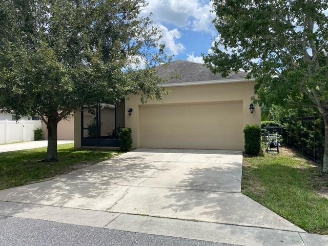A beige single-story house features a two-car garage, a concrete driveway, and surrounding trees — 15115 Pigeon Plum Lane, FL 34787, FL