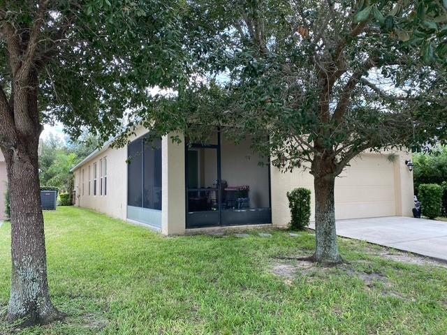 A beige house features a screened-in porch and a two-car garage under large shade trees — 15115 Pigeon Plum Lane, FL 34787, FL