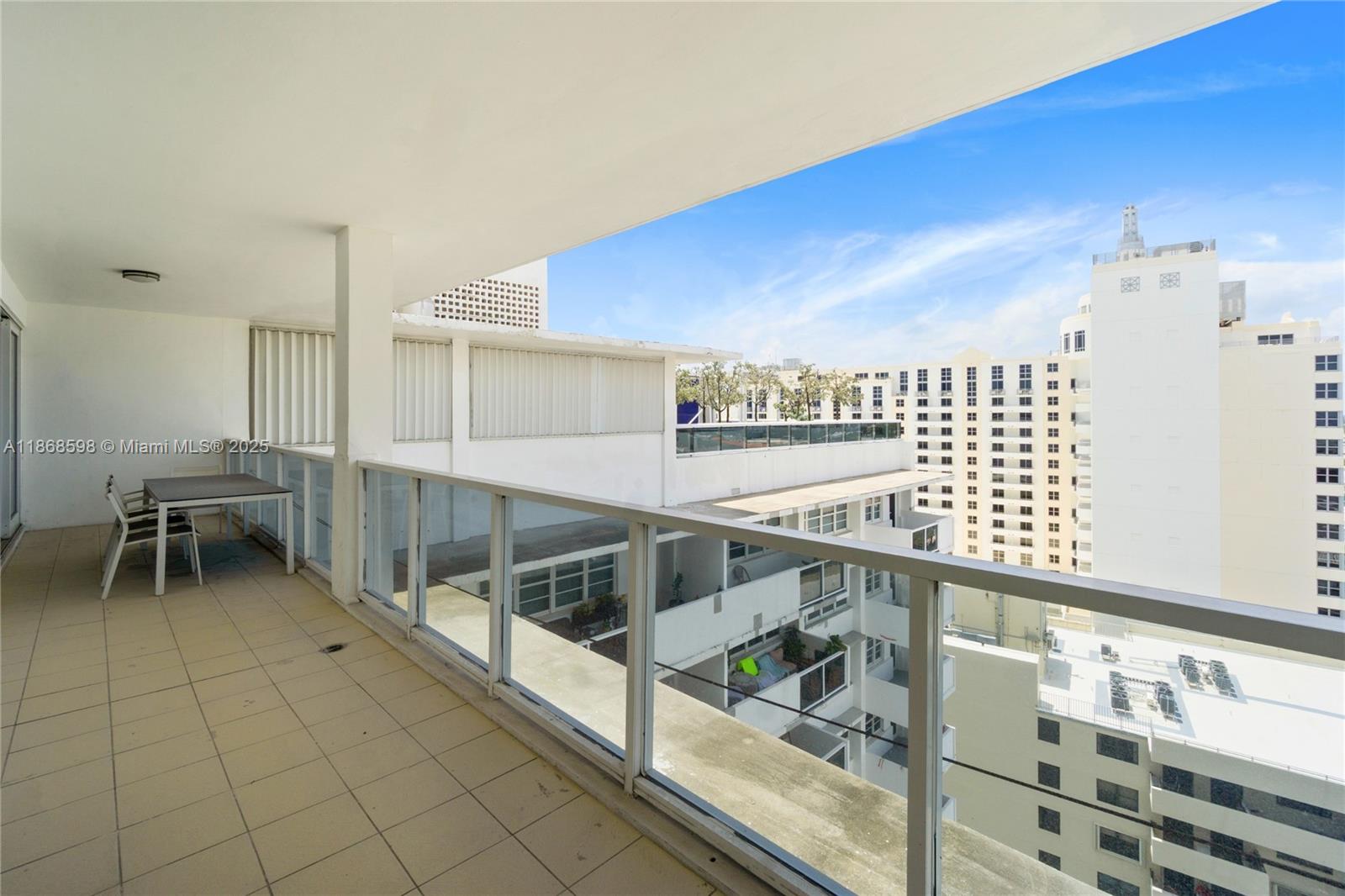 A spacious balcony with tile flooring, a dining set, and glass railings overlooks city buildings — 100 Lincoln Rd, Miami Beach FL 33139, MIAMI BEACH, FL