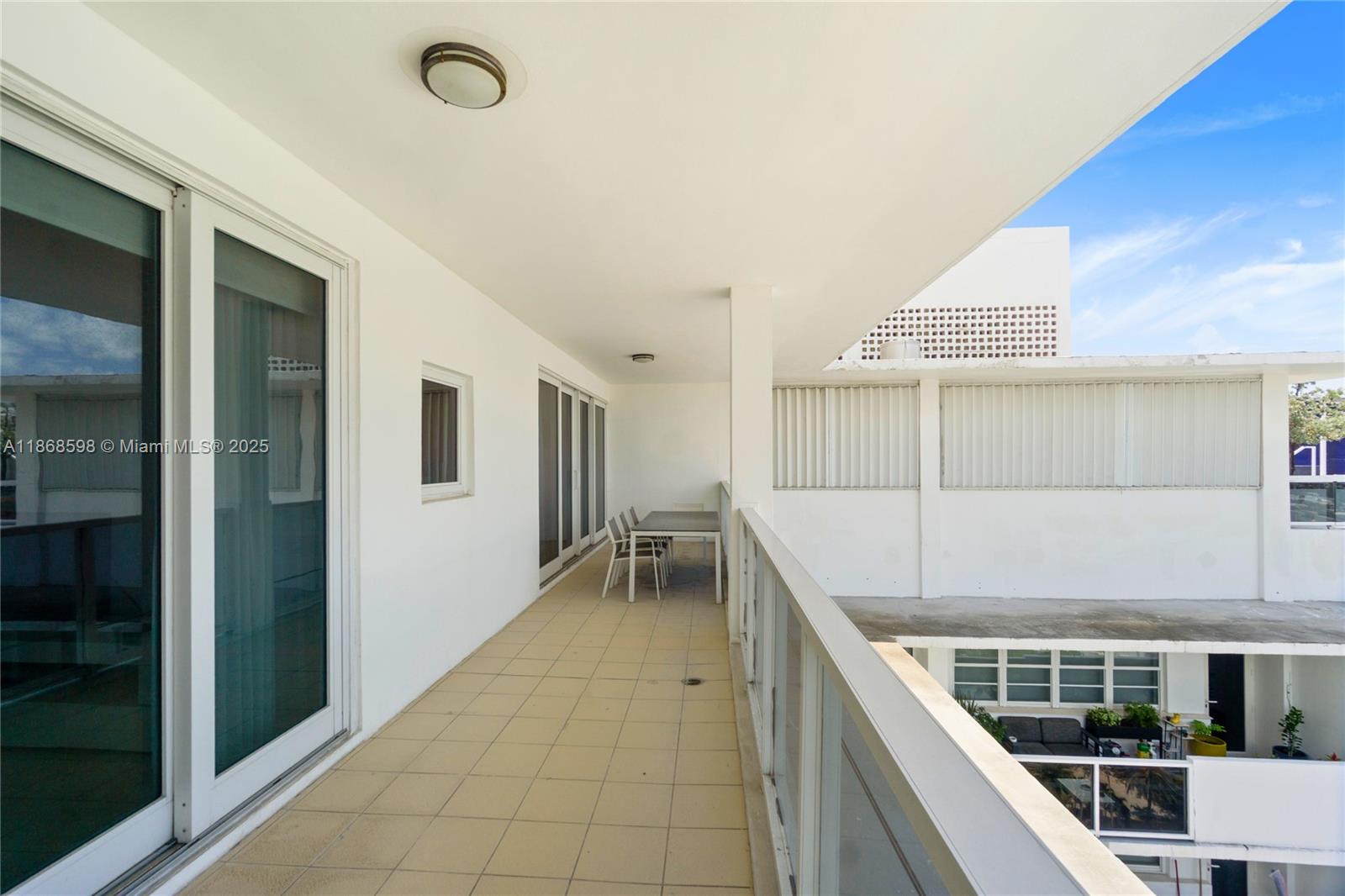 A long, tiled balcony features a dining set and glass railings overlooking a lower courtyard — 100 Lincoln Rd, Miami Beach FL 33139, MIAMI BEACH, FL