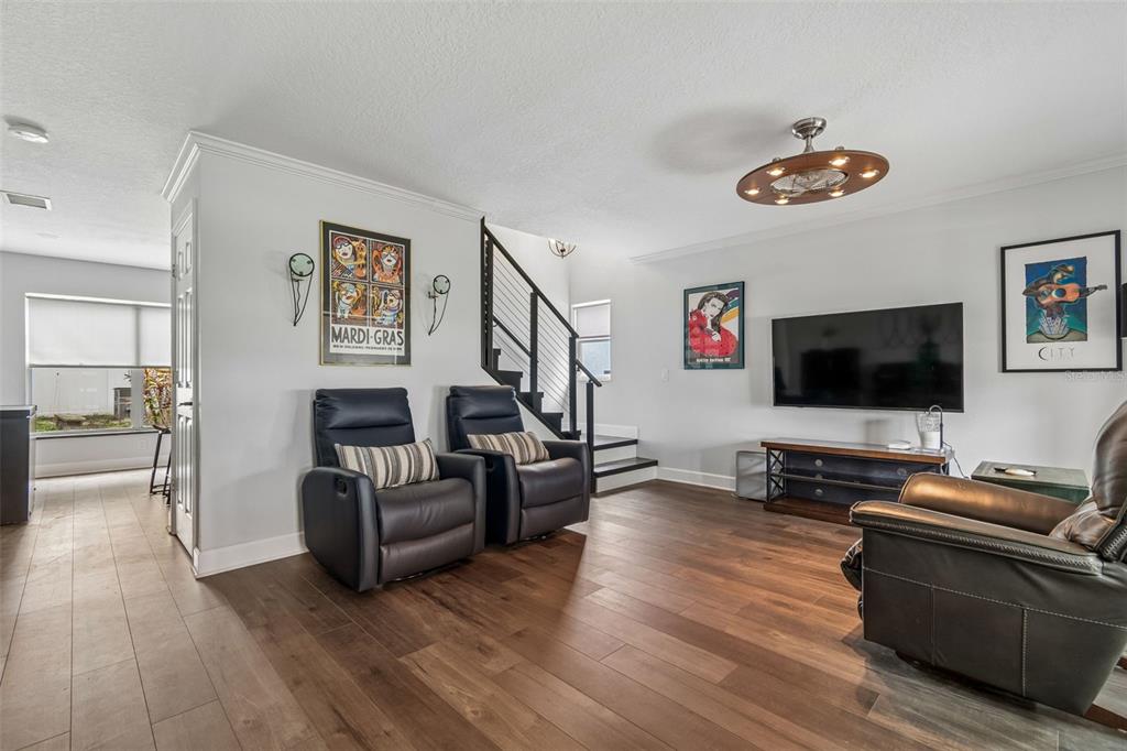A living room features dark leather recliners, wood-look flooring, a wall-mounted television, and a staircase — 2442 SAGEMONT DRIVE, BRANDON, FL