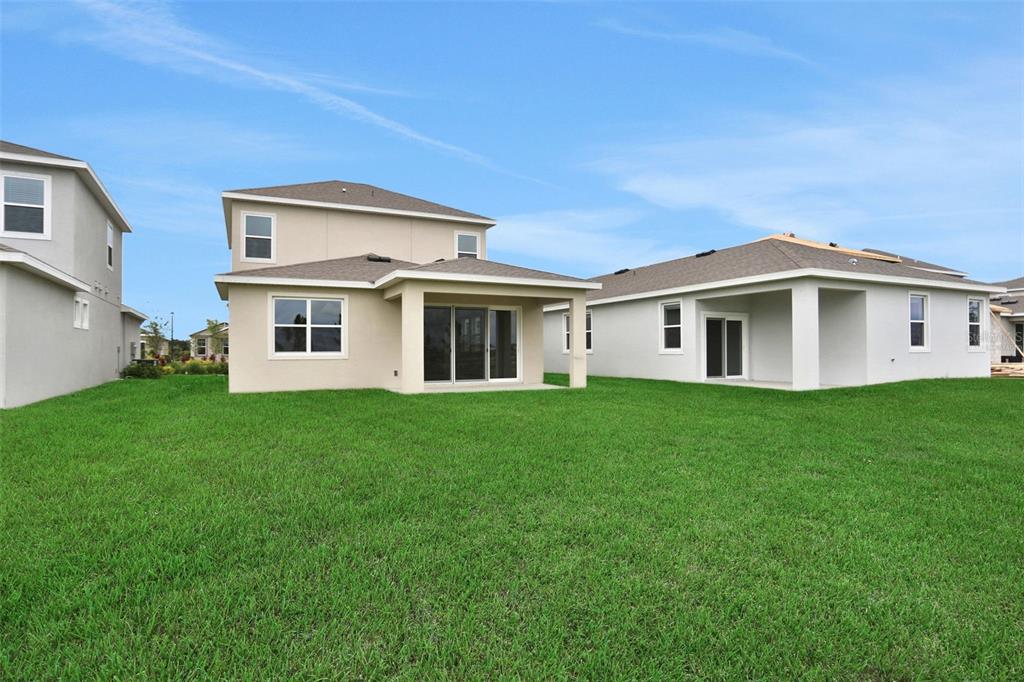 The rear exterior of two suburban houses features beige stucco siding, covered patios, and lawns — 8090 SUNNY POINT TRAIL, PARRISH, FL