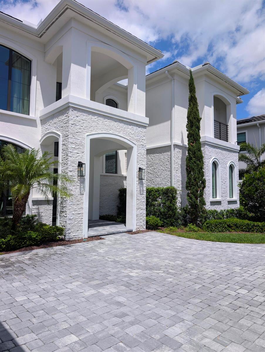 The exterior of a two-story white house features stone veneer, arched entryways, and a paver driveway — 7080 NW 26th Way, Boca Raton FL 33496, BOCA RATON, FL