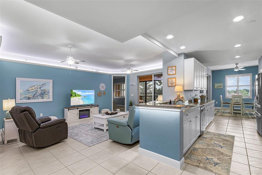 An open-concept living room and kitchen featuring blue walls, tile flooring, and white cabinetry — 24399 BALTIC AVENUE UNIT 202, PUNTA GORDA, FL