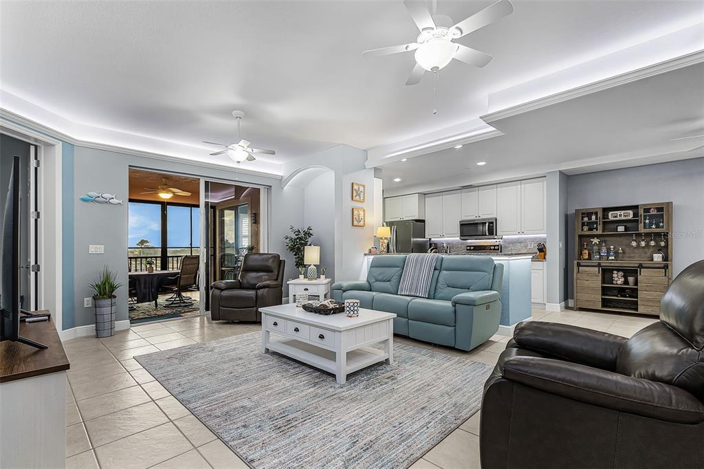 A living room with a blue sofa, two leather recliners, and an open-concept kitchen — 24399 BALTIC AVENUE UNIT 202, PUNTA GORDA, FL