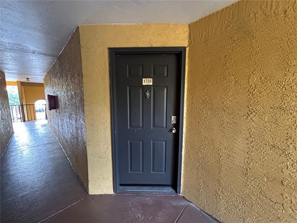A dark gray front door with the number 1735 is set in a yellow textured wall — 4512 COMMANDER DRIVE UNIT 1735, ORLANDO, FL
