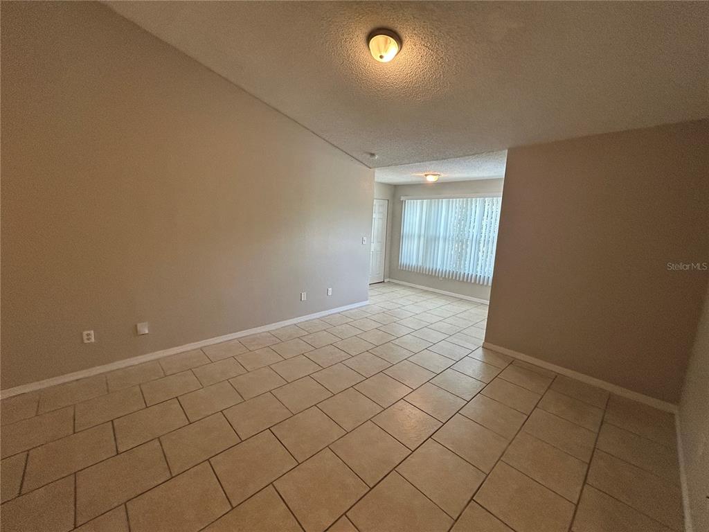 An empty living room features vaulted ceilings, beige walls, and light-colored tile flooring — 4512 COMMANDER DRIVE UNIT 1735, ORLANDO, FL