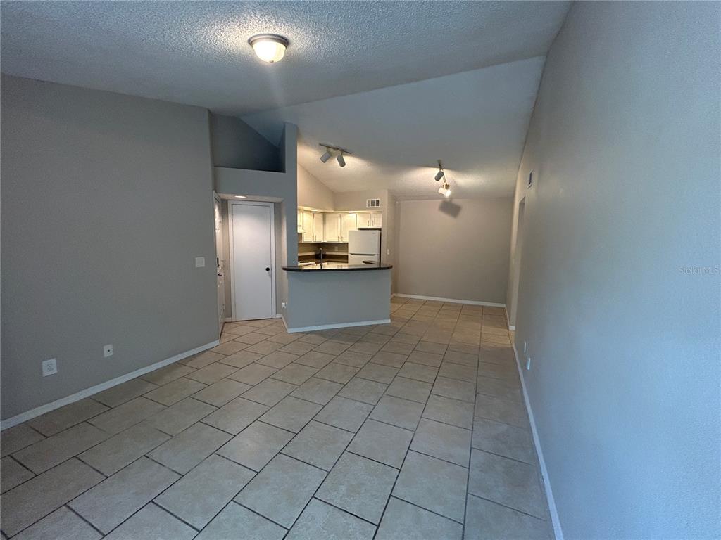 An open-concept living area features light-colored tile flooring, vaulted ceilings, and a kitchen pass-through — 4512 COMMANDER DRIVE UNIT 1735, ORLANDO, FL