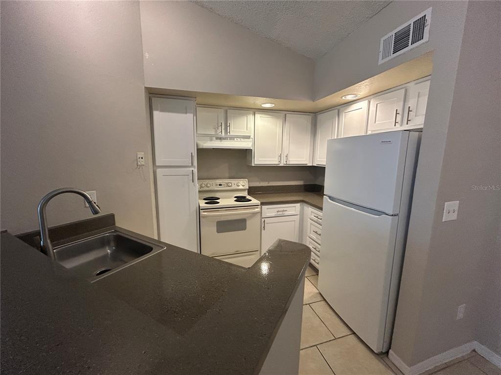 A kitchen features white cabinetry, a white stove, a white refrigerator, and dark countertops — 4512 COMMANDER DRIVE UNIT 1735, ORLANDO, FL