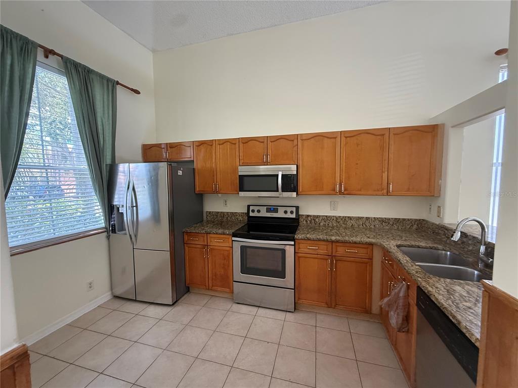 A kitchen features wood cabinets, granite countertops, stainless steel appliances, and tile flooring — 6711 GREEN ISLAND CIRCLE, LAKE WORTH, FL