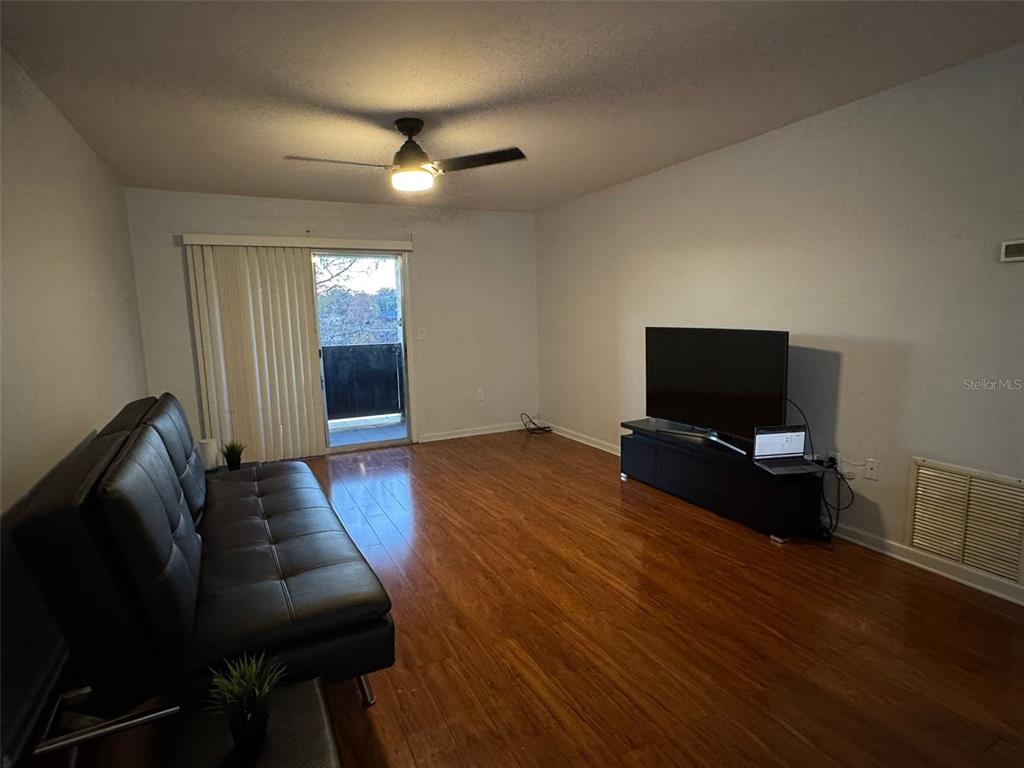 A living room features hardwood floors, a black sofa, a television stand, and a sliding door — 912 LAKE DESTINY ROAD UNIT G, ALTAMONTE SPRINGS, FL