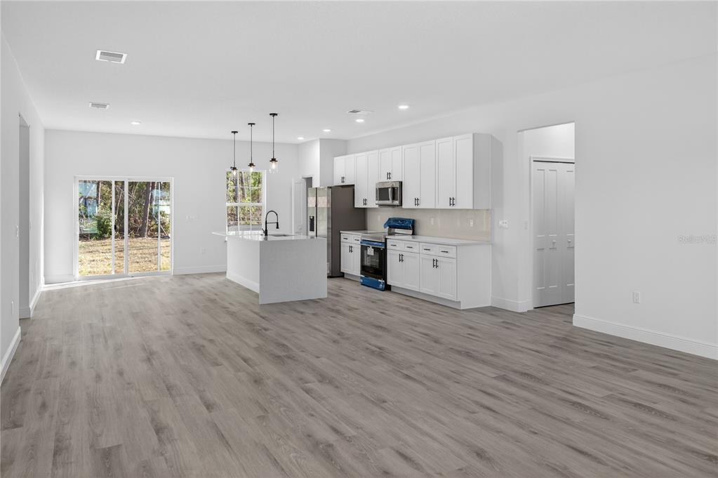 A bright, open-concept kitchen and living area featuring white cabinets, an island, and wood-look flooring — 3272 W FAIRBANK DRIVE, CITRUS SPRINGS, FL