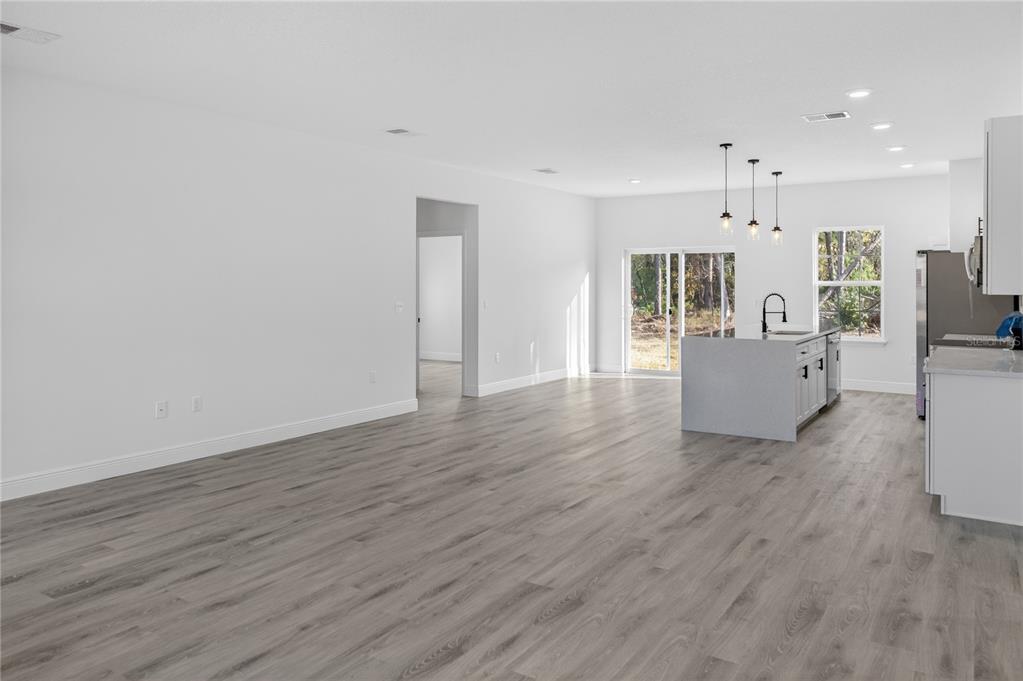 An open-concept living area features light gray wood-look flooring, white walls, and a kitchen island — 3272 W FAIRBANK DRIVE, CITRUS SPRINGS, FL