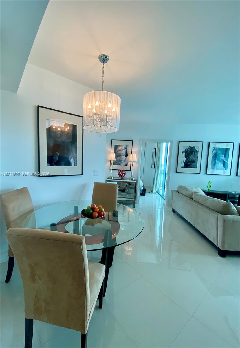 A dining area with a glass table, upholstered chairs, and a chandelier opens to a living room — 350 S Miami Ave # 3813, Miami FL 33130, MIAMI, FL