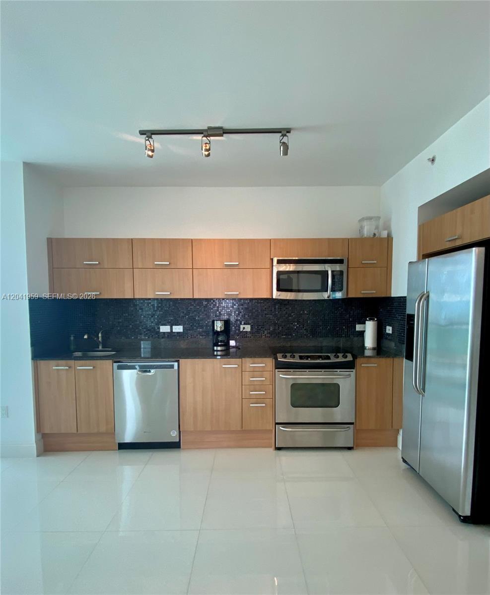 A modern kitchen features light wood cabinets, stainless steel appliances, and a dark tiled backsplash — 350 S Miami Ave # 3813, Miami FL 33130, MIAMI, FL