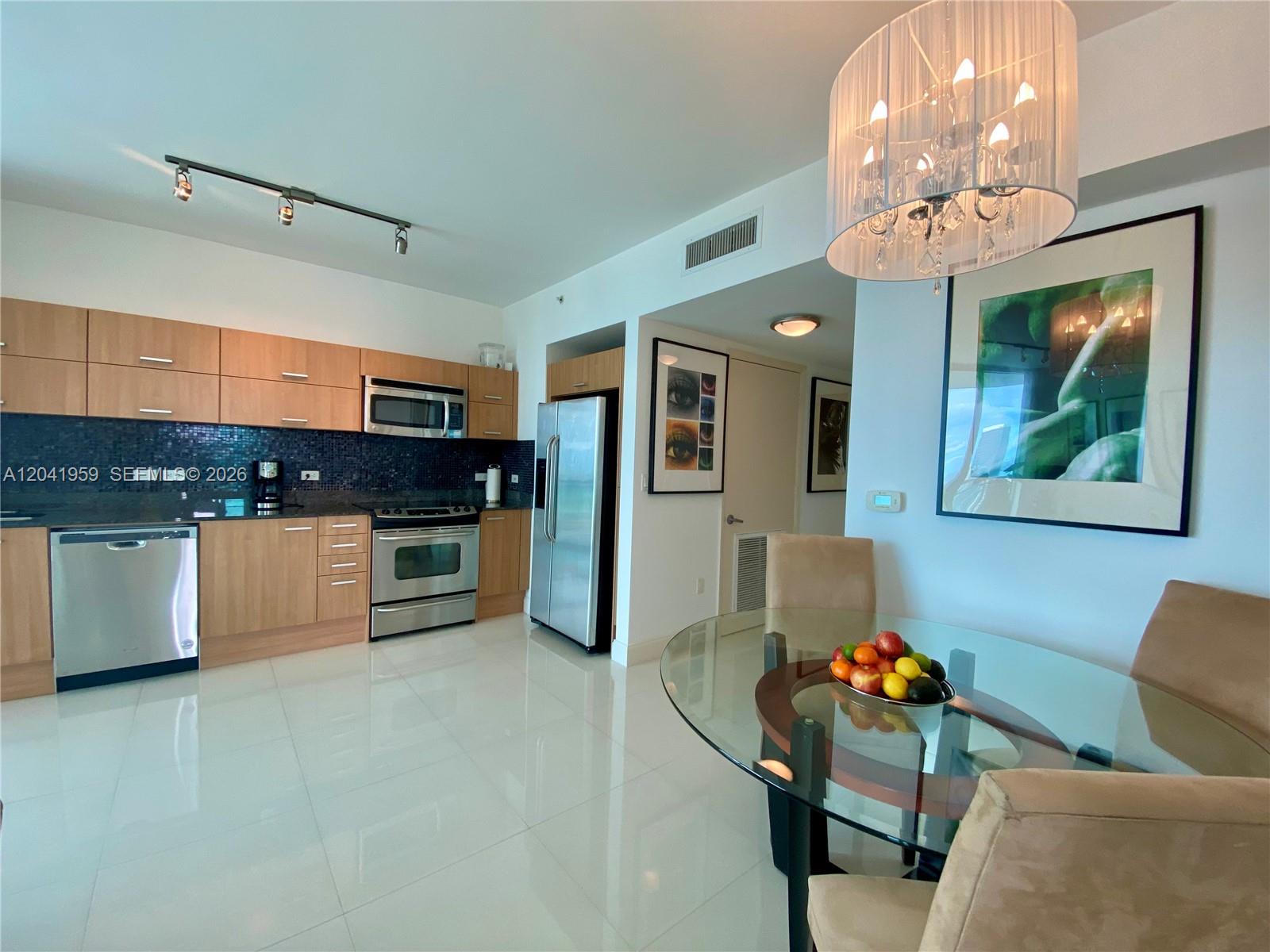 A modern kitchen with light wood cabinets and stainless steel appliances opens to a dining area — 350 S Miami Ave # 3813, Miami FL 33130, MIAMI, FL