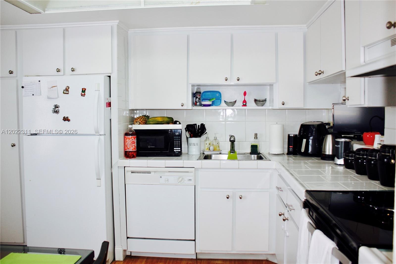 A kitchen features white cabinets, white appliances, and tiled countertops — 18555 NE 14th Ave # 702A, Miami FL 33179, MIAMI, FL