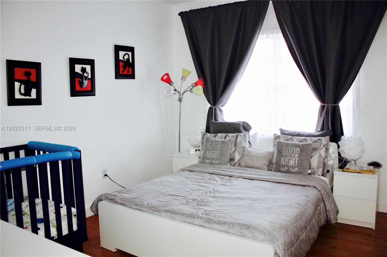 A bedroom features a bed with grey bedding, a dark blue crib, and dark curtains — 18555 NE 14th Ave # 702A, Miami FL 33179, MIAMI, FL