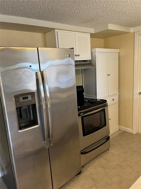 A kitchen features stainless steel appliances, white cabinetry, and light-colored tile flooring — 3632 PENSDALE DRIVE, NEW PORT RICHEY, FL