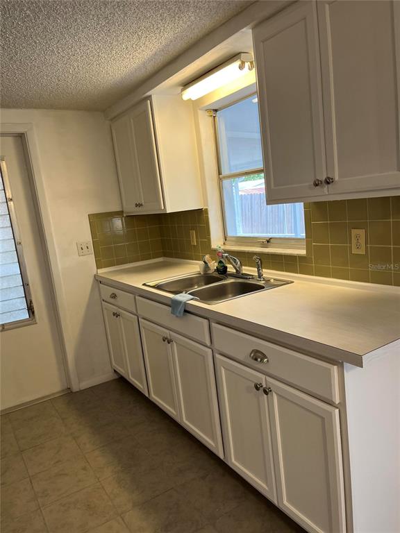 A kitchen features white cabinets, a double-basin sink, and olive green tiled backsplashes — 3632 PENSDALE DRIVE, NEW PORT RICHEY, FL