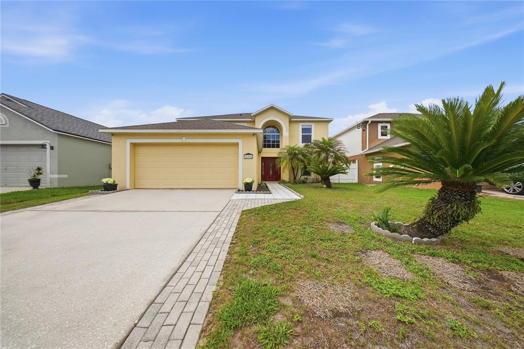 A two-story yellow stucco house features a two-car garage and a paved walkway — 24945 RAVELLO STREET, LAND O LAKES, FL