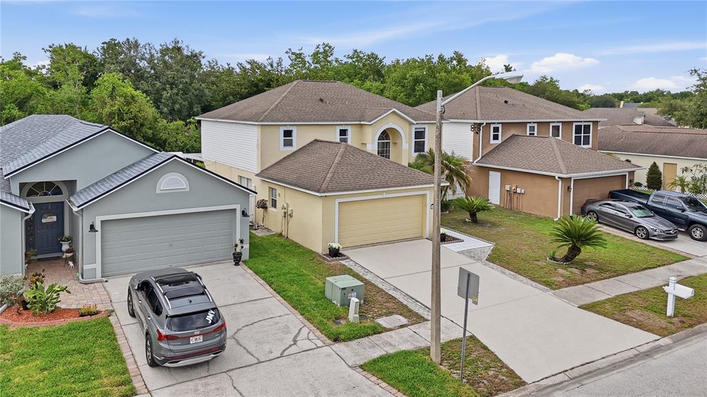 An aerial view shows three suburban houses with driveways, garages, and green lawns — 24945 RAVELLO STREET, LAND O LAKES, FL