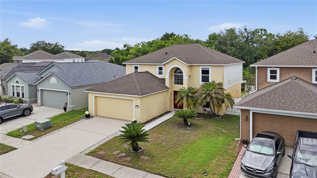 An exterior view of a two-story yellow house with a two-car garage and palm trees — 24945 RAVELLO STREET, LAND O LAKES, FL