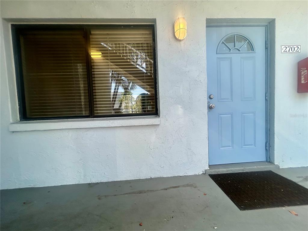 A light blue front door and a window with blinds on a white stucco exterior — 5310 26TH STREET W UNIT 2702, BRADENTON, FL