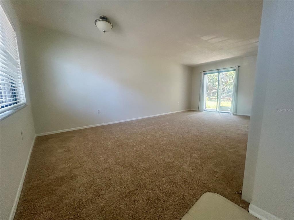 An empty room with beige carpeting, light-colored walls, a ceiling light, and sliding glass doors — 5310 26TH STREET W UNIT 2702, BRADENTON, FL