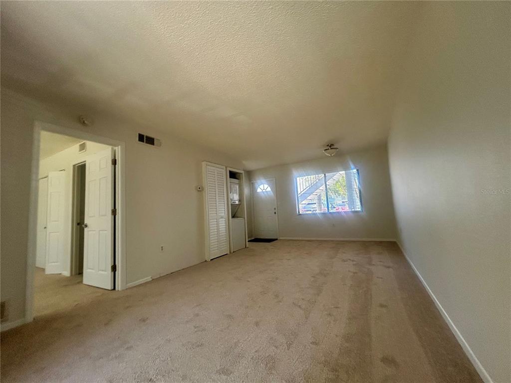 An interior view of a carpeted living room with a closet, laundry area, and window — 5310 26TH STREET W UNIT 2702, BRADENTON, FL