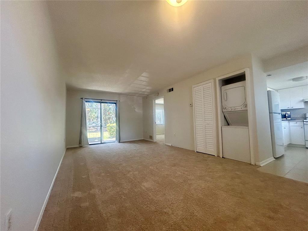 A carpeted living room features a sliding glass door, a laundry closet, and an adjacent kitchen — 5310 26TH STREET W UNIT 2702, BRADENTON, FL