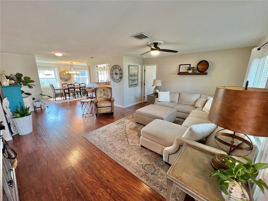 An open-concept living and dining area features hardwood floors, a sectional sofa, and neutral decor — 9359 CASA GRANDE AVENUE, ENGLEWOOD, FL