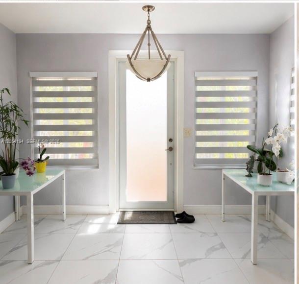 A bright entryway features a glass-paneled door, two white tables, and marble-look tile flooring — 741 NE 81st St, Miami FL 33138, MIAMI, FL