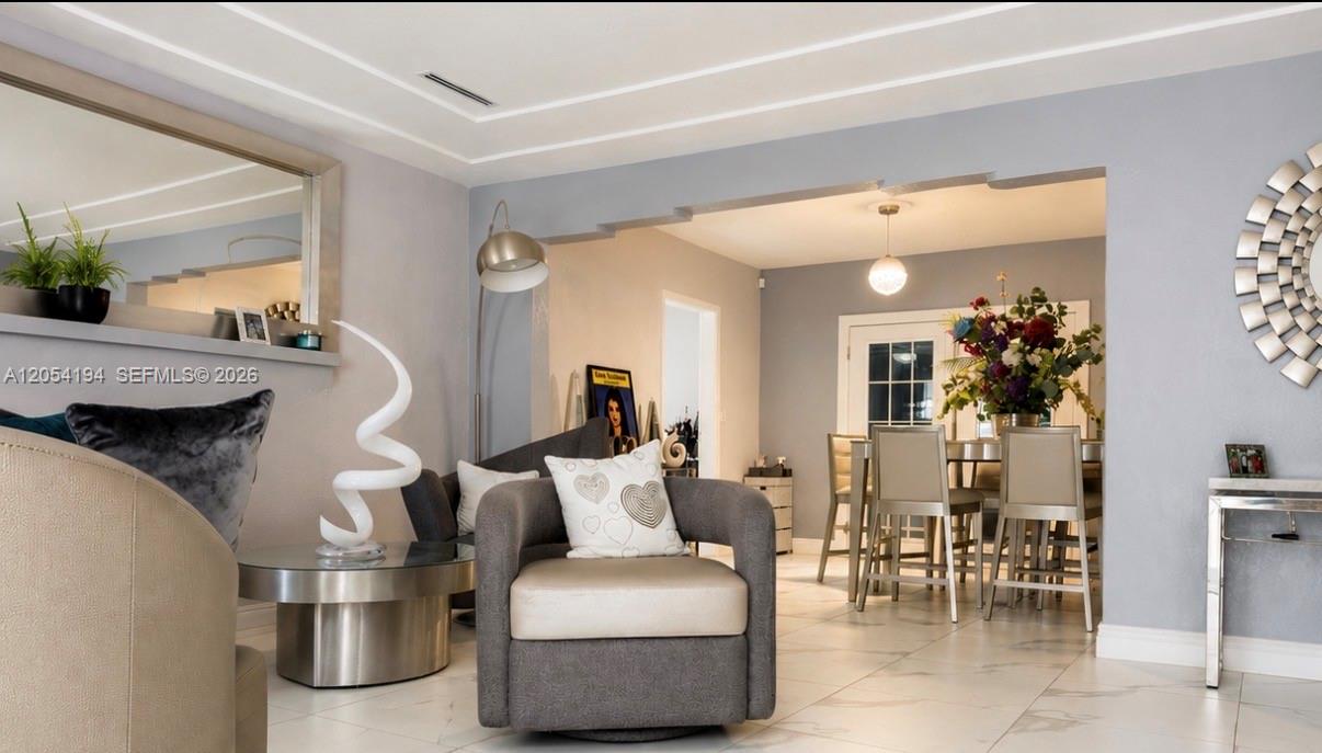 A living room with a gray armchair, a glass coffee table, and an adjacent dining area — 741 NE 81st St, Miami FL 33138, MIAMI, FL