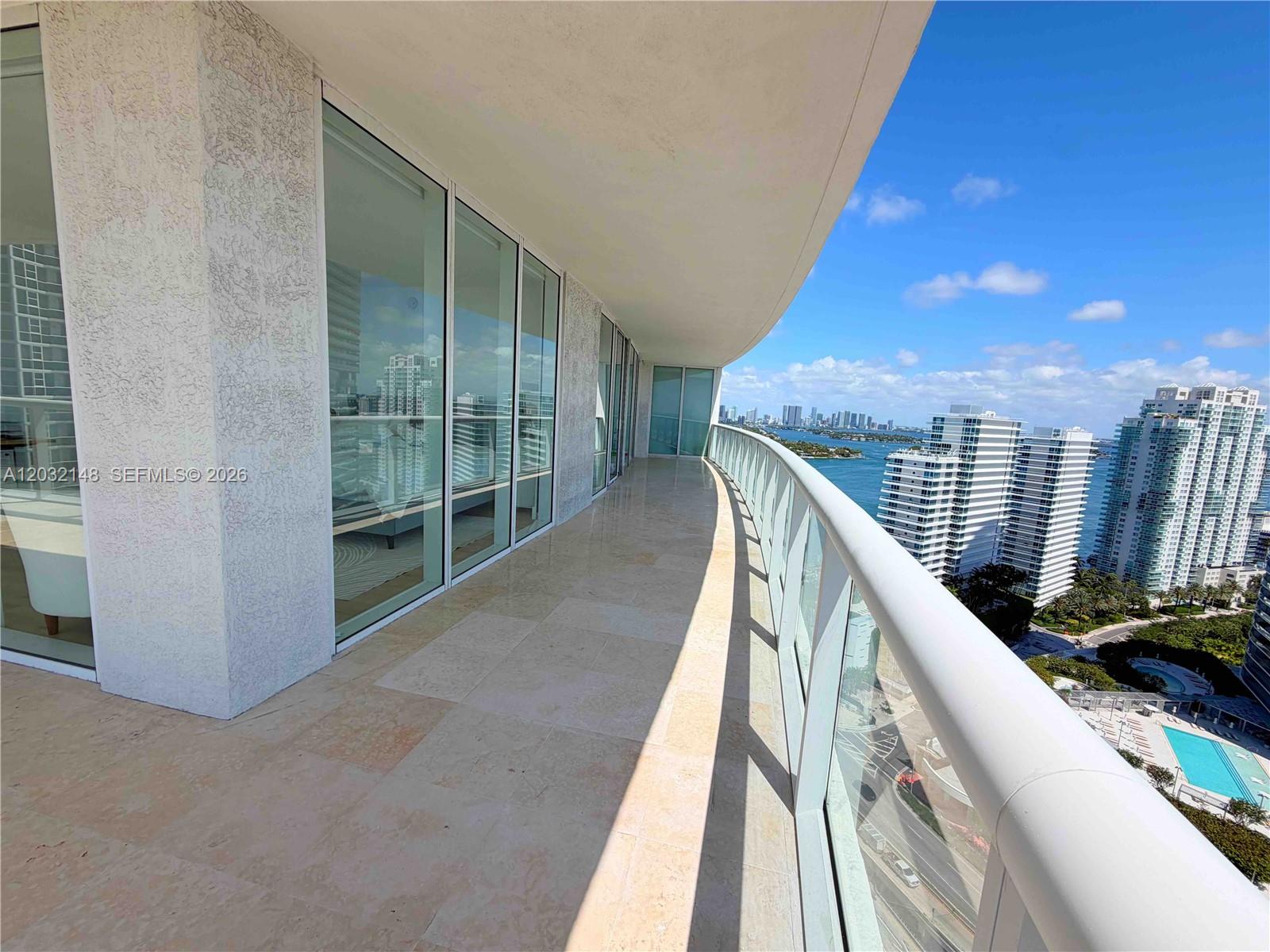 A curved balcony with stone flooring and a glass railing overlooks a coastal city skyline — 450 Alton Rd # 2610, Miami Beach FL 33139, MIAMI BEACH, FL