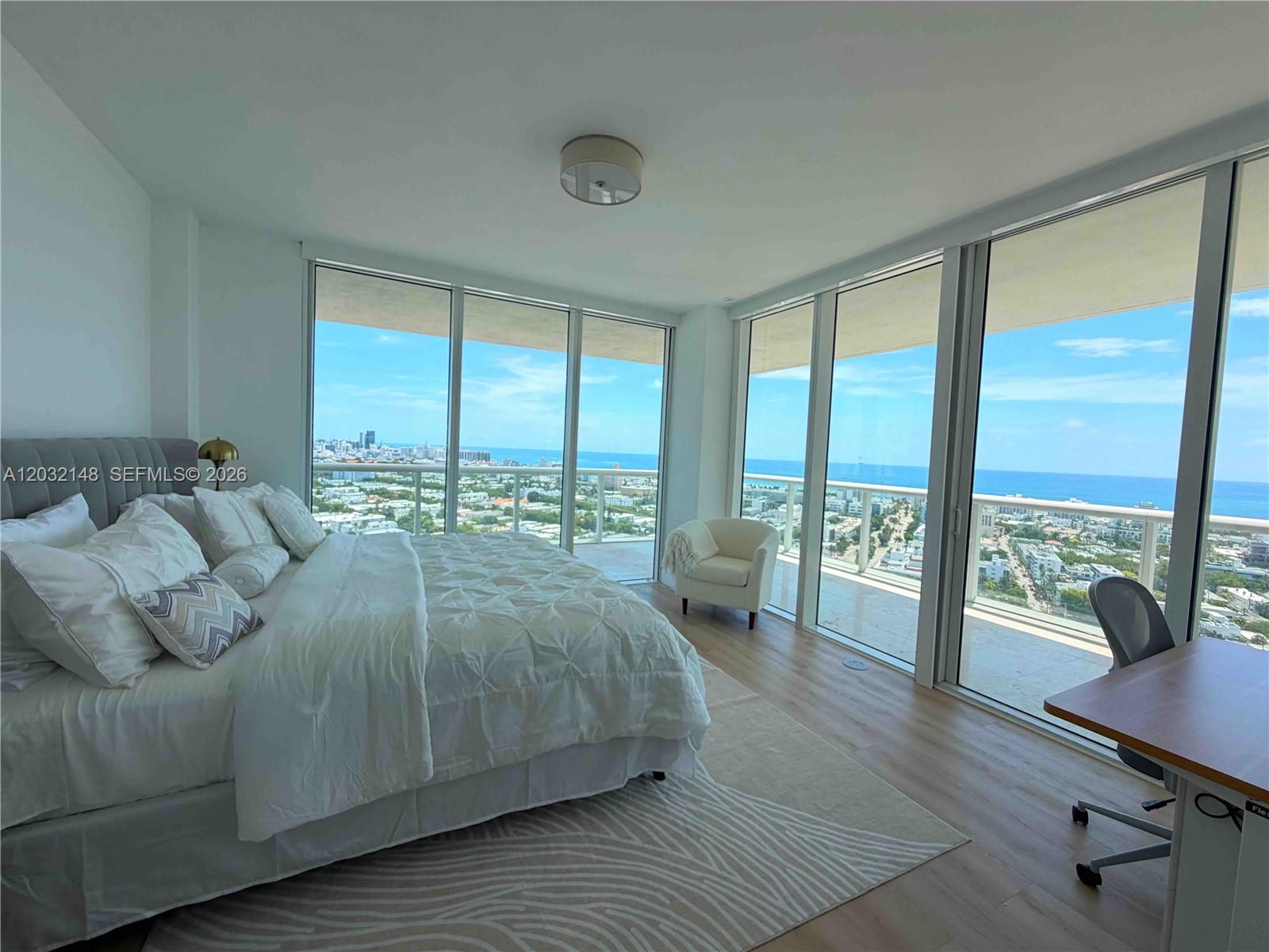 A bedroom features floor-to-ceiling windows with ocean views, light wood flooring, and a white bed — 450 Alton Rd # 2610, Miami Beach FL 33139, MIAMI BEACH, FL