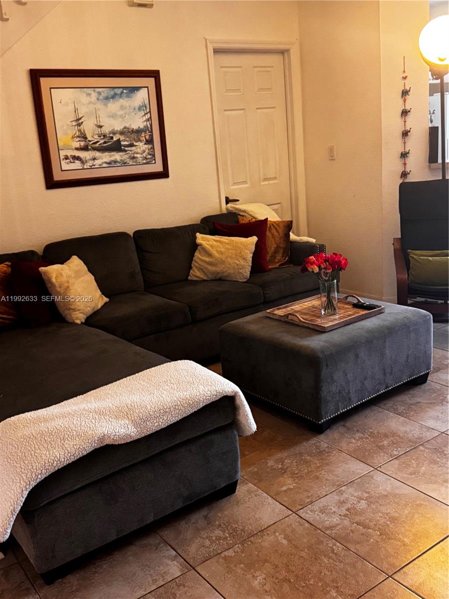 A living room features a dark gray sectional sofa, matching ottoman, and tiled flooring — 10723 NW 85th Ter # 38, Doral FL 33178, DORAL, FL