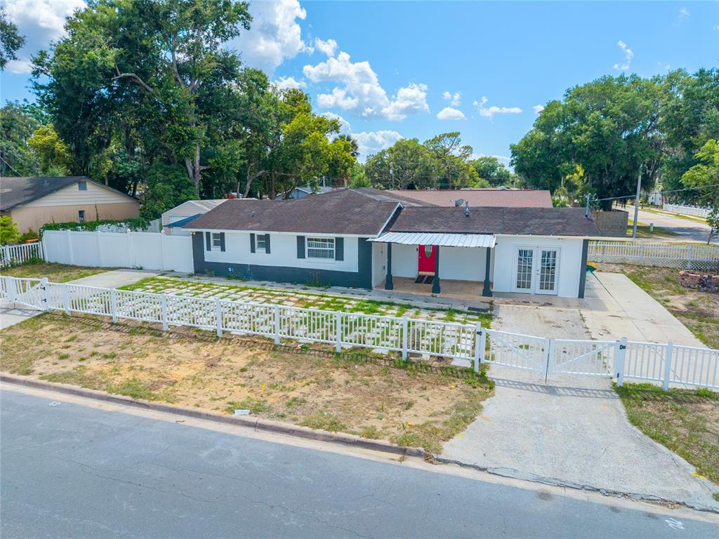 A single-story house with a white fence, a red front door, and a concrete driveway — 1230 E 1ST AVENUE, MOUNT DORA, FL