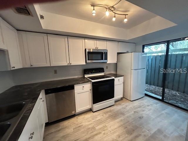 A kitchen features white cabinets, dark countertops, stainless steel appliances, and light wood-look flooring — 5647 SUMMER SIDE LANE UNIT 41A, SARASOTA, FL