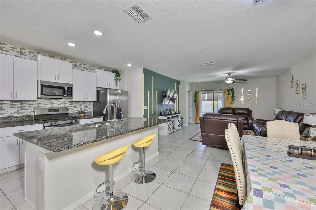 An open-concept kitchen with a granite island and bar stools overlooks a living room — 10335 SHADY PRESERVE DRIVE, RIVERVIEW, FL