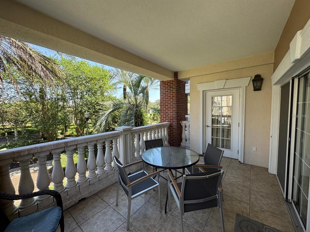 A covered balcony features a glass-topped table, four chairs, a stone balustrade, and exterior views — 7651 WHISPER WAY UNIT 201, KISSIMMEE, FL