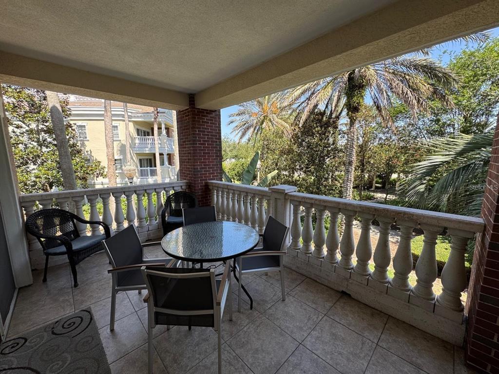 A covered balcony features a round glass table, chairs, and a stone balustrade railing — 7651 WHISPER WAY UNIT 201, KISSIMMEE, FL
