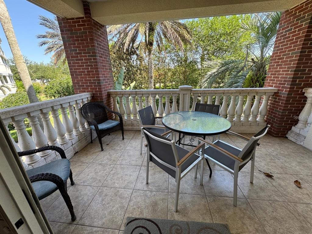 A covered balcony features brick columns, a stone balustrade, tile flooring, and patio furniture — 7651 WHISPER WAY UNIT 201, KISSIMMEE, FL