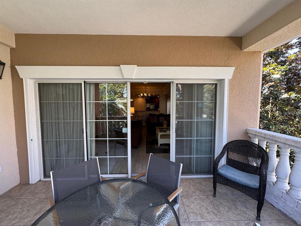 A balcony with tile flooring, patio furniture, and sliding glass doors leading into a living area — 7651 WHISPER WAY UNIT 201, KISSIMMEE, FL