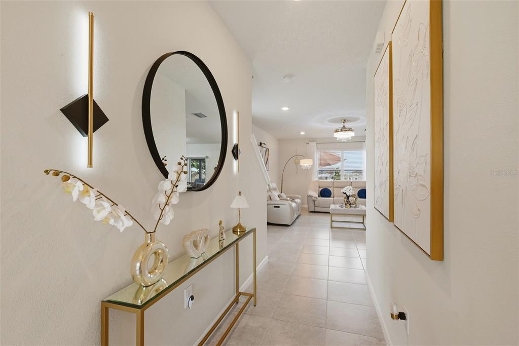 A bright entryway features a glass console table, a round mirror, and wall art — 7603 TAORMINA WAY, CLERMONT, FL