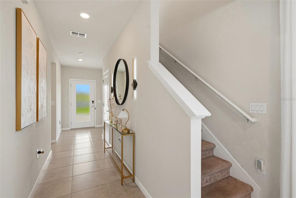 A bright entryway features a tiled floor, a console table, and stairs with carpeted steps — 7603 TAORMINA WAY, CLERMONT, FL