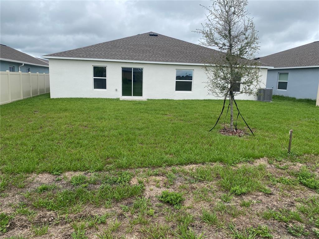 The backyard of a single-story house features a white stucco exterior, sliding glass doors, and lawn — 2125 LASSO LOOP, EAGLE LAKE, FL