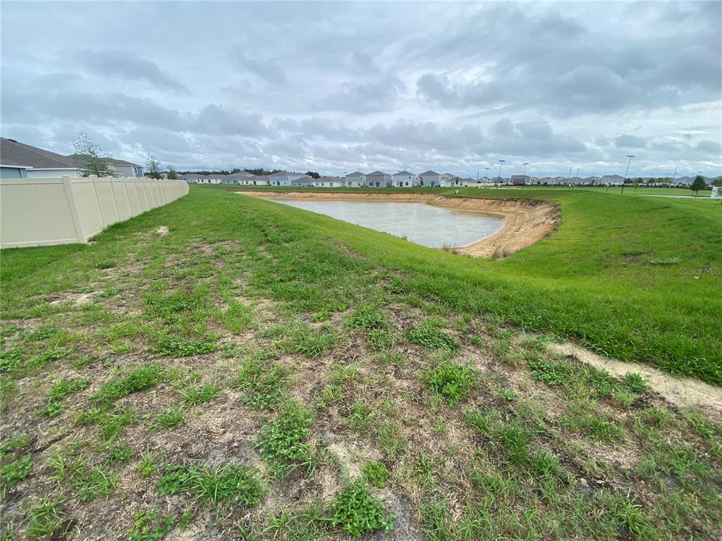 A grassy yard slopes down toward a retention pond behind a residential fence — 2125 LASSO LOOP, EAGLE LAKE, FL